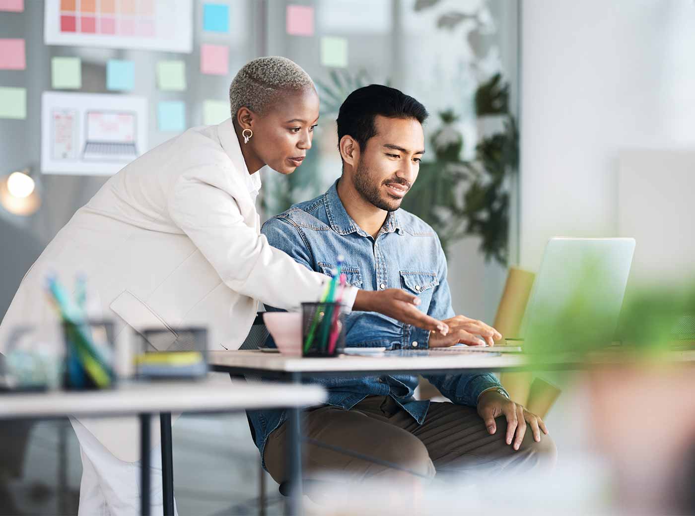 In an office setting, the image shows a lady and a man working together on a laptop.